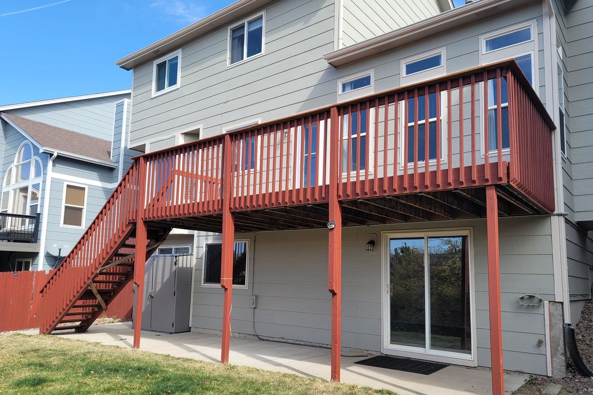 Raised wood deck with red-stained railings behind a home